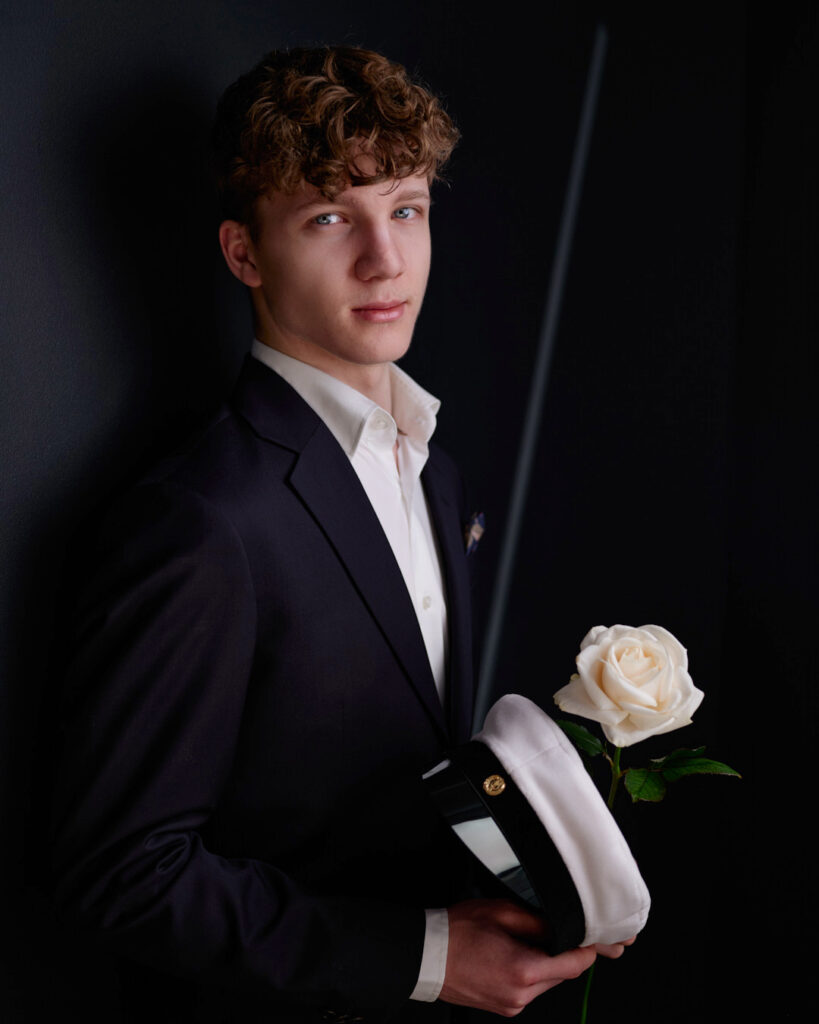Ylioppilaskuva nuoresta miehestä ilman kravattia, valkoinen ruusu ja valkolakki