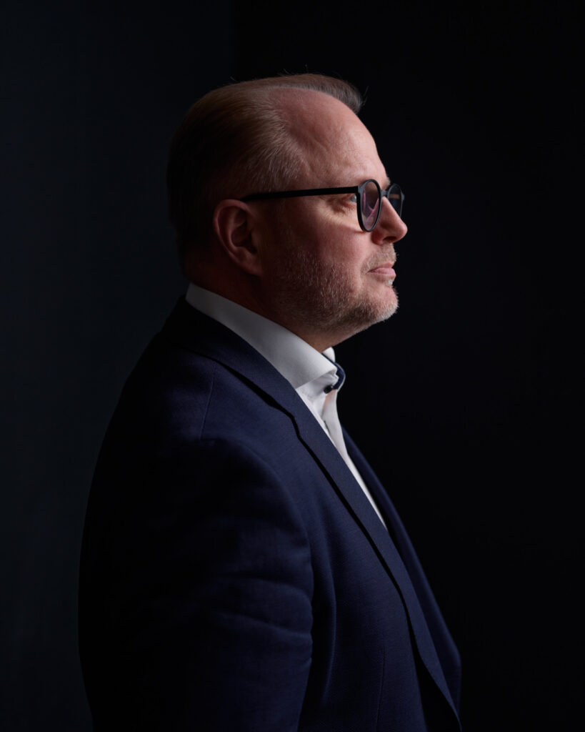 Tyylikäs CV-kuva – mies puvussa profiilissa tummaa taustaa vasten